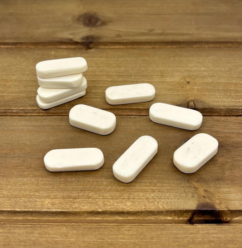 May include: A collection of small, rectangular, off-white objects, possibly erasers or decorative pieces, are scattered on a wooden surface. Some are stacked, while others are arranged individually. The objects have rounded edges and a smooth texture.