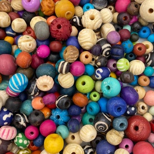 May include: A large collection of colorful wooden beads in various shapes and sizes. The beads are made of wood and have a natural finish. Some of the beads have patterns or designs carved into them.