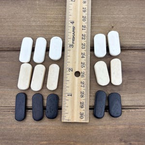 May include: A collection of small, rectangular wooden pieces in white, natural, and black arranged on a wooden surface. A ruler is placed vertically next to the pieces, showing measurements in inches.