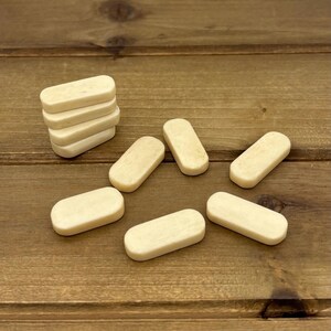 May include: A collection of small, rectangular, off-white game pieces. Some are stacked, while others are scattered on a wooden surface. The pieces have rounded edges and a smooth texture, suggesting they are made of bone or a similar material.