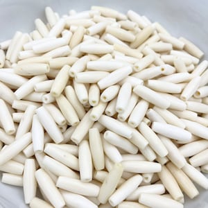 May include: A bowl filled with white, smooth, cylindrical beads. The beads are made of bone and have a natural, slightly off-white color.