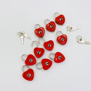 May include: A set of ten red heart-shaped padlocks with silver keys. The padlocks are small and have a simple design.