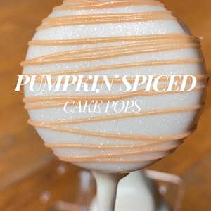 May include: A single pumpkin spiced cake pop with white frosting and orange drizzle. The cake pop is on a white stick. The words "PUMPKIN SPICED CAKE POPS" are written on the front of the cake pop.