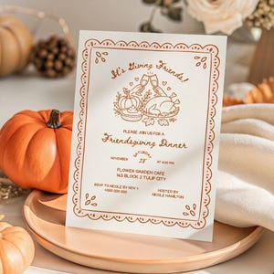 May include: A white rectangular invitation card with copper-coloured text and illustrations. The text reads: It's Giving Friends! Please join us for a Friendsgiving Dinner, Saturday November 28th at 6:00 PM, Flower Garden Cafe, 143 Block 2 Tulip City.
