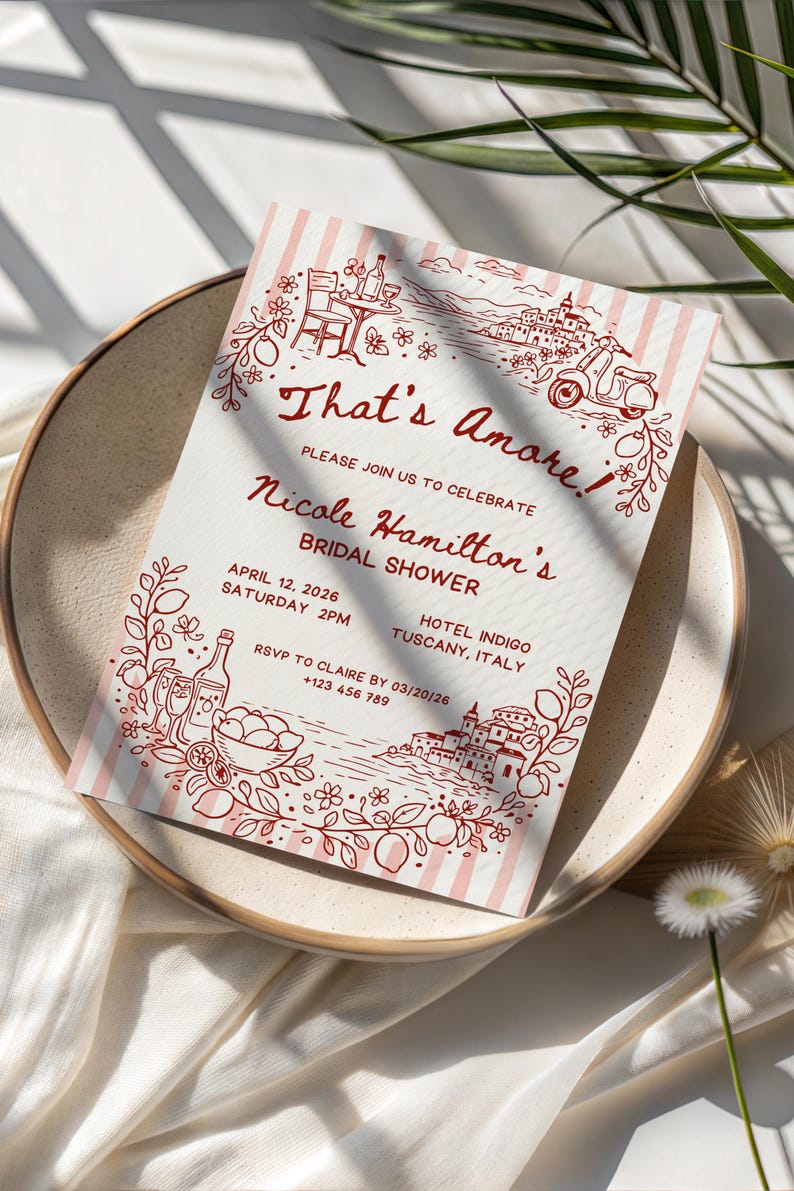 May include: A bridal shower invitation with the words "That's Amore" in a decorative font. The invitation features a red and white striped background and illustrations of Italian scenery. The invitation is on a beige plate.