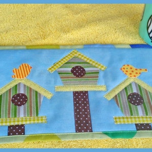 May include: A blue fabric coaster with three birdhouses and yellow birds. Each birdhouse has a brown, white, and green striped pattern with a brown polka dot center.