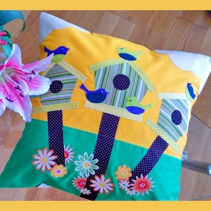 May include: A yellow pillow with a green, blue and yellow birdhouse design. The pillow features a variety of colourful birds and flowers.