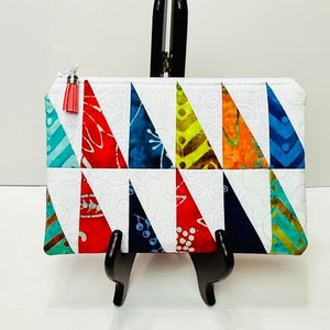 May include: A white zippered pouch with a colourful geometric pattern of triangles. The pouch is made of fabric and has a tassel zipper pull.