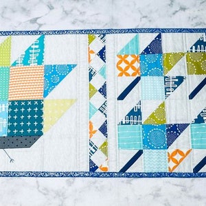 May include: A patchwork quilt featuring a turkey design on one side and a geometric pattern on the other. The turkey is made from various blue, green, yellow, and orange fabrics. The geometric pattern is made from blue, green, and orange fabrics.