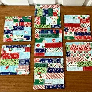 以下が含まれることがあります： 7つの正方形のクリスマスをテーマにした布コースターのコレクション。各コースターは、赤、緑、白、青の生地を使用したパッチワークデザインが特徴です。コースターには、雪の結晶、キャンディケーン、その他の休日のモチーフが施されています。