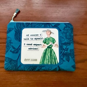 May include: Teal zipped pouch with a floral pattern and a white square featuring a vintage illustration of a woman in a green dress and the text "of course I talk to myself. I need expert advice!"