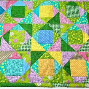 May include: A colourful patchwork quilt with a geometric pattern of squares and triangles. The quilt is made of various fabrics in shades of green, pink, blue, and yellow.
