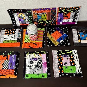 May include: A collection of nine square fabric coasters featuring various Halloween-themed patchwork patterns in orange, black, purple, and green. The designs include motifs of bats, spiders, candy corn, and ghosts. A silver Canada Dry soda can sits on one.