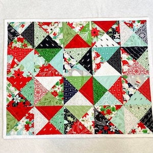 May include: A red, green, white and black patchwork quilt with a white border. The quilt is made of small triangles and has a Christmas theme.