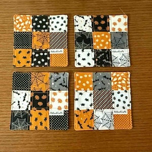 Puede incluir: Cuatro posavasos cuadrados con temática de Halloween con diseños de patchwork. Cada posavasos presenta una variedad de patrones que incluyen telarañas, murciélagos, lunares y rayas en naranja, negro, blanco y gris. Los posavasos están colocados sobre una superficie de madera.