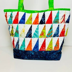 May include: A white quilted tote bag with a green top and a blue bottom. The bag is decorated with colorful triangular patches.