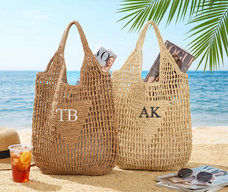 Puede incluir: Dos bolsos de mano tejidos en tonos beige y marr&oacute;n claro sobre una playa de arena. Cada bolso tiene un dise&ntilde;o de tejido abierto grande, un asa y un bolsillo con iniciales bordadas. Se ven revistas dentro de los bolsos. Gafas de sol y una bebida en primer plano.