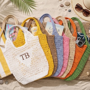 Puede incluir: Una colecci&oacute;n de bolsos tote de crochet calado de colores, en blanco, amarillo, marr&oacute;n, azul, rosa y naranja. Cada bolso tiene un asa a juego. Algunos bolsos contienen art&iacute;culos como una revista, protector solar y una c&aacute;mara. Tema de playa.
