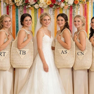 Puede incluir: Una novia y sus damas de honor posan con bolsos de mano tejidos con iniciales. La novia lleva un vestido de novia blanco, y las damas de honor visten vestidos a juego. El fondo presenta decoraciones coloridas.