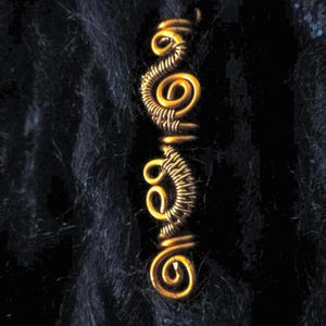 Op de afbeelding: Dreadlock kralen van gouden draad met een spiraalvormig ontwerp. De kralen zijn gemaakt van draad dat is gedraaid en gevormd tot een spiraalvorm. De kralen zijn een populair accessoire voor dreadlocks.