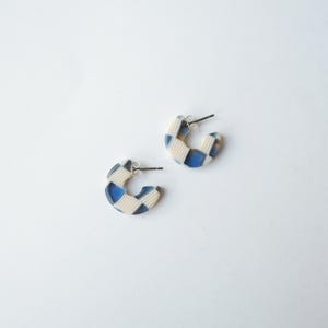 May include: A pair of hoop earrings with a blue, white, and cream checkered pattern. The earrings have silver posts and are set against a white background. The earrings are a modern accessory.