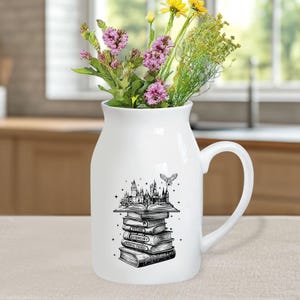 May include: A white ceramic pitcher with a handle, filled with colorful flowers. The pitcher features a black and white illustration of a castle, books, and a flying owl. The books have the words "Potions", "Herbology", and "Magical Theory".