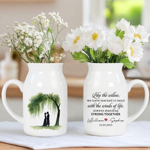 May include: Two white ceramic vases with handles, each holding white flowers. One vase features a green weeping willow tree with a couple under it. The other vase has text that reads "Like the willow, always standing STRONG TOGETHER".