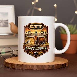Op de afbeelding: Witte keramische mok met een gedetailleerde afbeelding. Het ontwerp bevat een longhorn, olieboren en de tekst "CTT OIL EXPLORATION & CATTLE". De mok heeft een gebogen handvat en staat op een houten onderzetter.