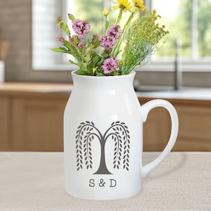 Puede incluir: Jarrón de cerámica blanca con un diseño de sauce llorón gris y las iniciales "S & D". El jarrón está lleno de una variedad de flores coloridas. El jarrón tiene un asa y está sobre una superficie neutra.