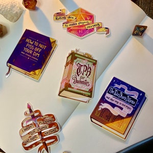 Puede incluir: Una colección de pegatinas con ilustraciones de dados, libros y una espada. Las pegatinas tienen un estilo caprichoso y de dibujos animados y presentan texto como "How to Not Piss Off Your DM" y "TPH for Dummies".