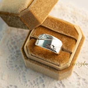 May include: A silver ring made from a spoon, displayed in a gold velvet ring box. The ring features floral and scrollwork details. The ring box is open, revealing the ring against a soft, neutral background. The word "everyday" is in the image.