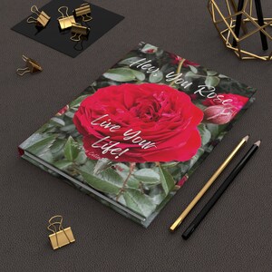 Puede incluir: Una rosa roja con hojas verdes en un diario blanco con el texto "Hey, you rose, live your life! The Rose Collection."