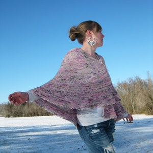 Op de afbeelding: Een vrouw draagt een roze en paarse gestreepte sjaal met een wit topje en blauwe jeans. Ze staat in een besneeuwd veld met een blauwe lucht op de achtergrond.