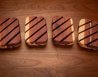 May include: Four wooden soap dishes with a striped design. The dishes are made of cedar wood and have a natural finish.