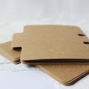 May include: A stack of brown paper dividers with rounded corners and three holes punched along the top edge. The dividers are designed for use in a binder or planner.