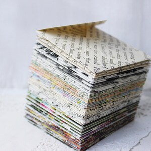 May include: A stack of folded paper envelopes, each made from a different page of a book, creating a colorful and textured pattern. The envelopes are stacked in a pyramid shape.