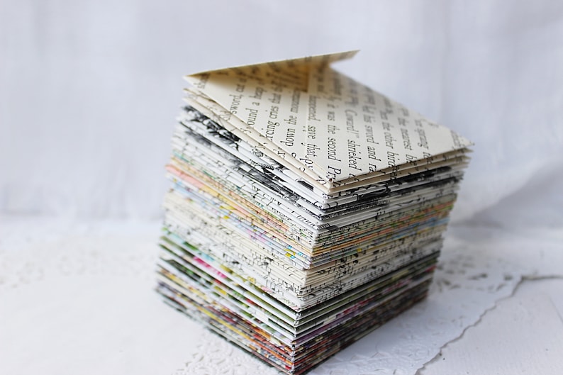 May include: A stack of folded paper envelopes, each made from a different page of a book, creating a colorful and textured pattern. The envelopes are stacked in a pyramid shape.