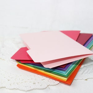 May include: A stack of colourful paper folders, with a pink folder on top. The folders are arranged in a rainbow pattern, with red, orange, yellow, green, blue, purple, and pink.