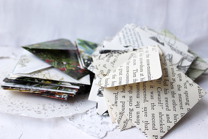 May include: A stack of folded paper envelopes made from recycled book pages. The envelopes are decorated with text and illustrations. The text on the envelopes reads: "g which Shce sprang to the nearest be uodn 15hen the other bira Fed his sword and ra 1! Coward!" shrieked up the snow-mountainy it was the second P his snow-shoes at hihappened, save that p d snow. Then the uno now the snow-covered a great crowd hea down the rcing cries tha again y e punogero PJO g-ting! ang hawks sont of th 245 the fou 'proms"