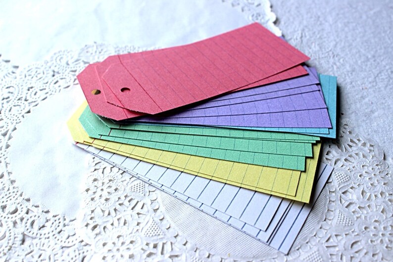 May include: A stack of colorful paper tags with lined paper. The tags are in shades of pink, purple, green, yellow, and white.
