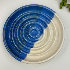 May include: A round ceramic dish featuring a concentric ribbed pattern. The surface is divided into two distinct colour sections, with one half glazed in a deep cobalt blue and the other half in a smooth, off-white cream finish.