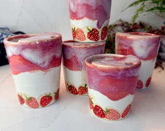 May include: A collection of five ceramic cups featuring a white base with a hand-painted strawberry pattern around the bottom and a glossy, drippy pink and white glaze finish on the upper portion. Each cup has a small notch on the rim.