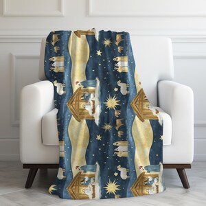 Könnte beinhalten: Eine blaue und goldene Kuscheldecke mit einem sich wiederholenden Muster der Weihnachtsgeschichte. Die Szene zeigt einen Holzstall, einen Stern und Figuren von Maria, Josef und dem Jesuskind.