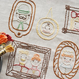 May include: Embroidered family portraits in various frame styles, including oval and square, are displayed on a neutral fabric. The portraits feature detailed stitching in brown, yellow, and red thread. Spools of embroidery floss are visible.