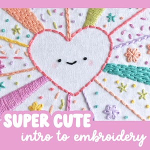 May include: Embroidered heart design with a smiling face, surrounded by colorful rays and floral accents. The text "SUPER CUTE intro to embroidery" is displayed in a pink banner at the bottom. The embroidery is on a white fabric background.