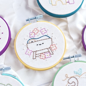 May include: Five embroidered hoop art pieces with various Christmas themes. The hoops are purple, teal, yellow, green, and purple. The designs include a star, a manger scene, a tree, and a bird.
