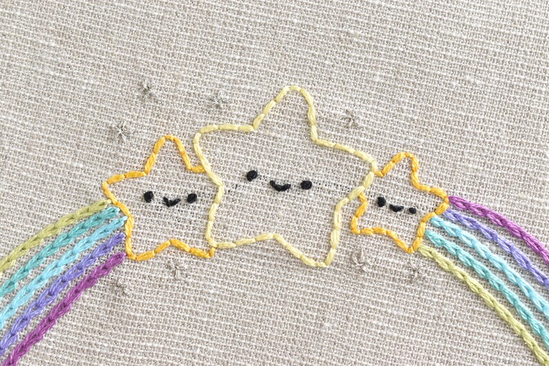 May include: Three yellow embroidered stars with black eyes and mouths, with a rainbow of purple, blue, and green thread stitched behind them.