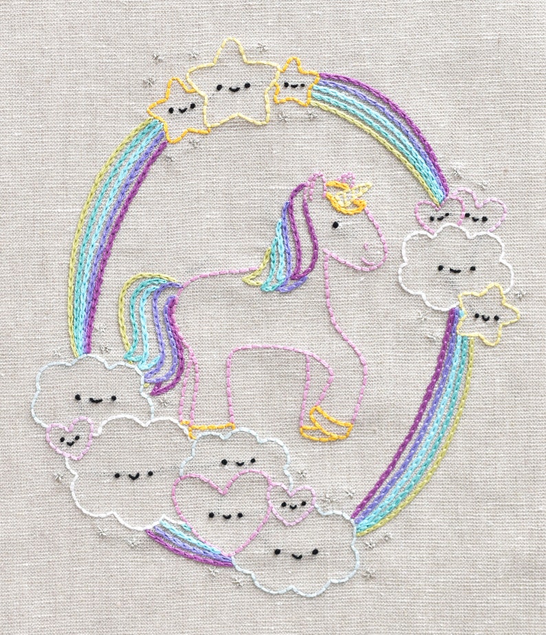 May include: Embroidered design of a unicorn standing on clouds with a rainbow arch above. The unicorn is pink and white with a yellow horn and mane. The clouds are white with smiling faces. The rainbow is multi-colored with a yellow, blue, and purple color scheme.
