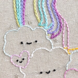 May include: Embroidered design of a rainbow with clouds and hearts. The clouds and hearts have smiling faces. The rainbow is made of multiple strands of yarn in different colors.