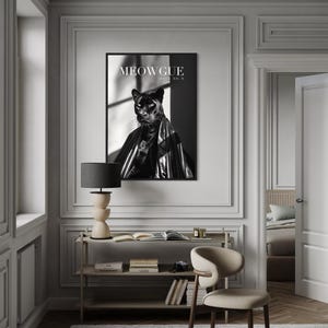 Peut inclure: Une impression encadrée en noir et blanc représentant une panthère vêtue d'une cape brillante. Le texte "MEOWGUE ISSUE NO. 9" est visible. L'impression est au-dessus d'une étagère avec des livres, une lampe et une chaise.